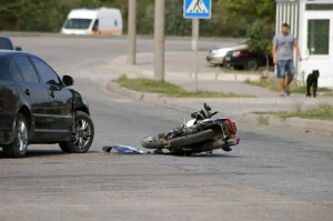A motorcyle on the ground that has been hit by a car. The rider is wondering if they can still receive compensation if they weren't wearing a helmet during the accident.